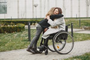 młoda kobieta, siedząca na wózku inwalidzkim aktywnym, uśmiechnięta i przytulająca dziecko z którym jest na spacerze